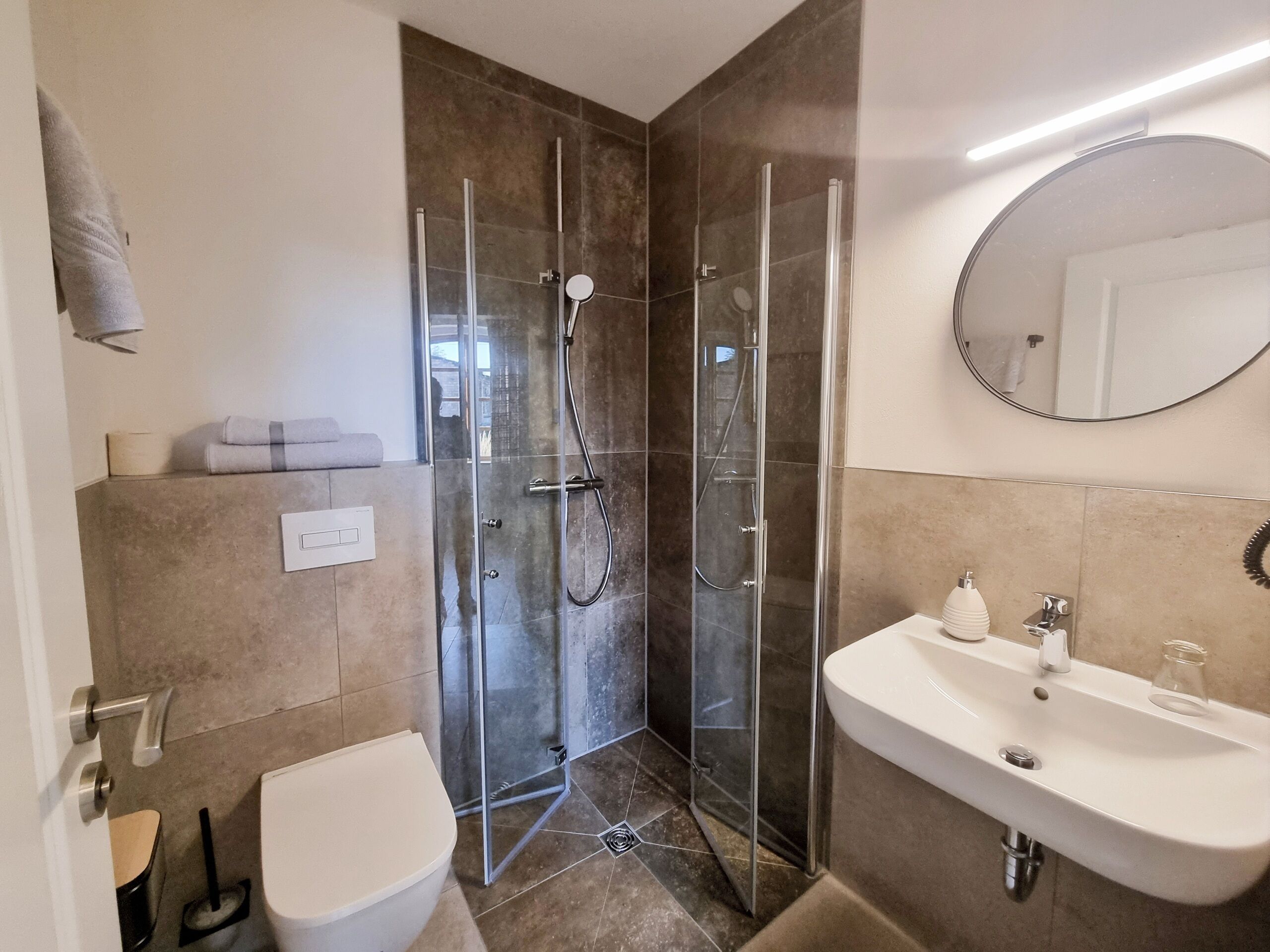 A modern bathroom with a glass-enclosed shower, a white sink with a mirror, and a toilet.