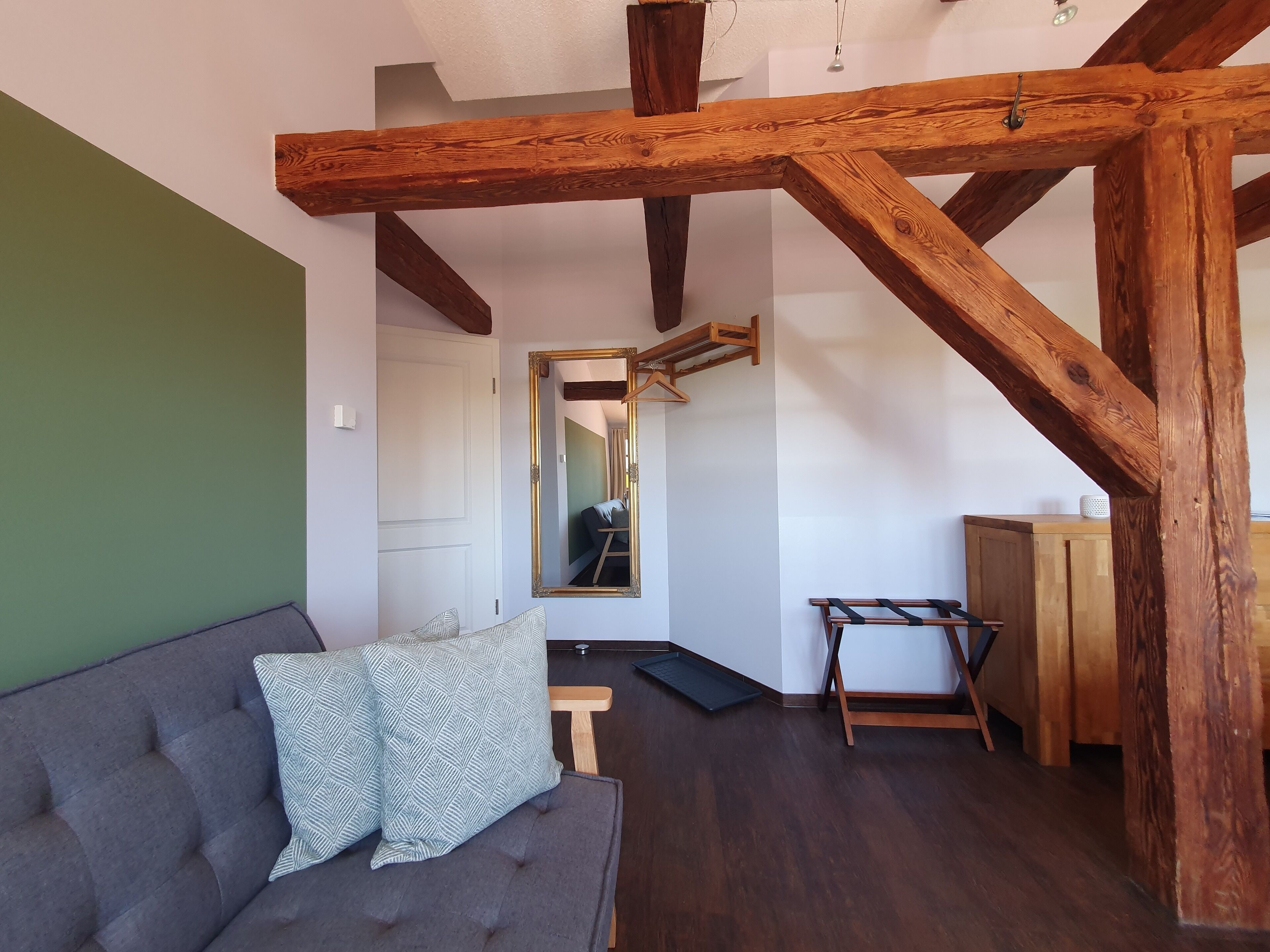 A room with a grey sofa, wooden beams, a mirror, and a wooden cabinet.