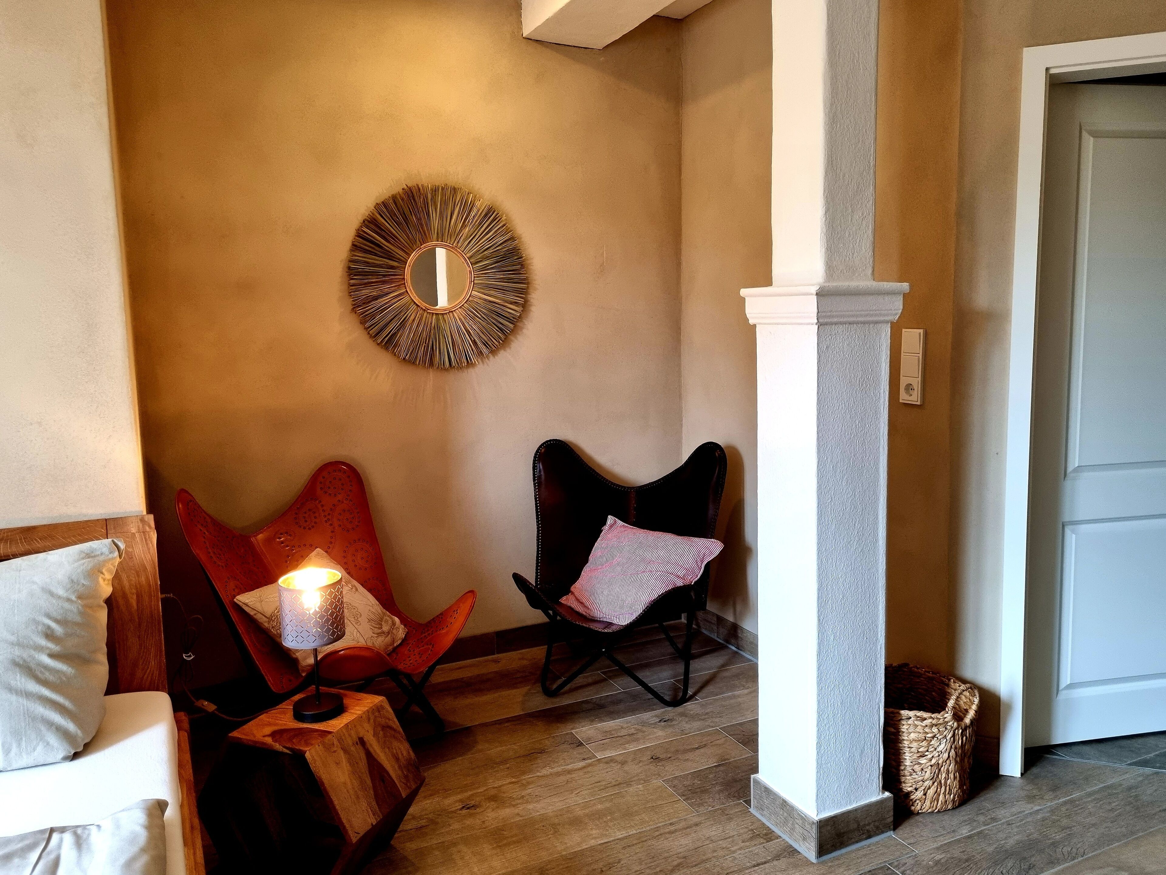 A cozy room with a wooden floor, a round mirror on the wall, a red chair with a cushion, and a white door.