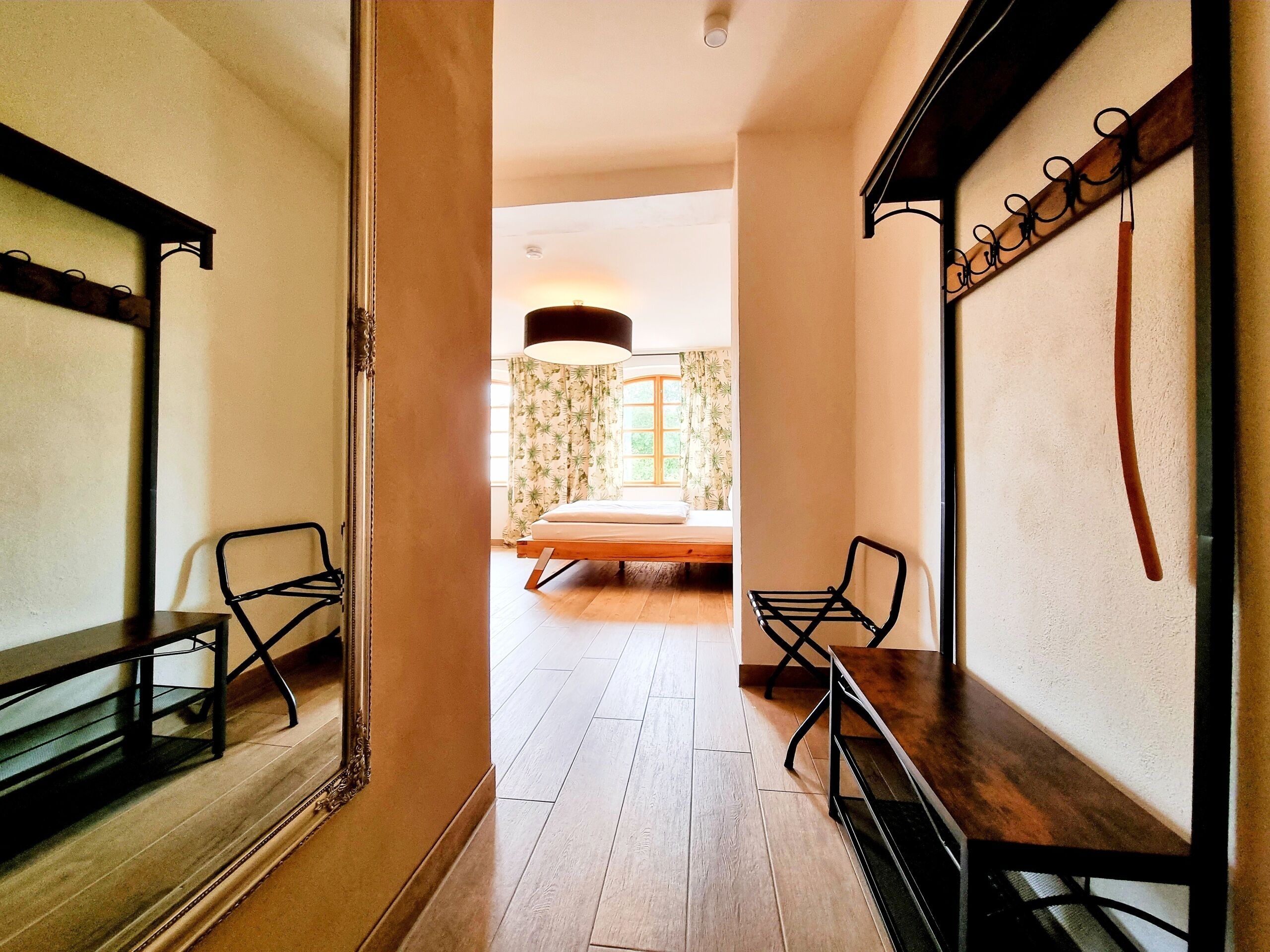 A room with a bed, two chairs, a large mirror, and a wooden floor.