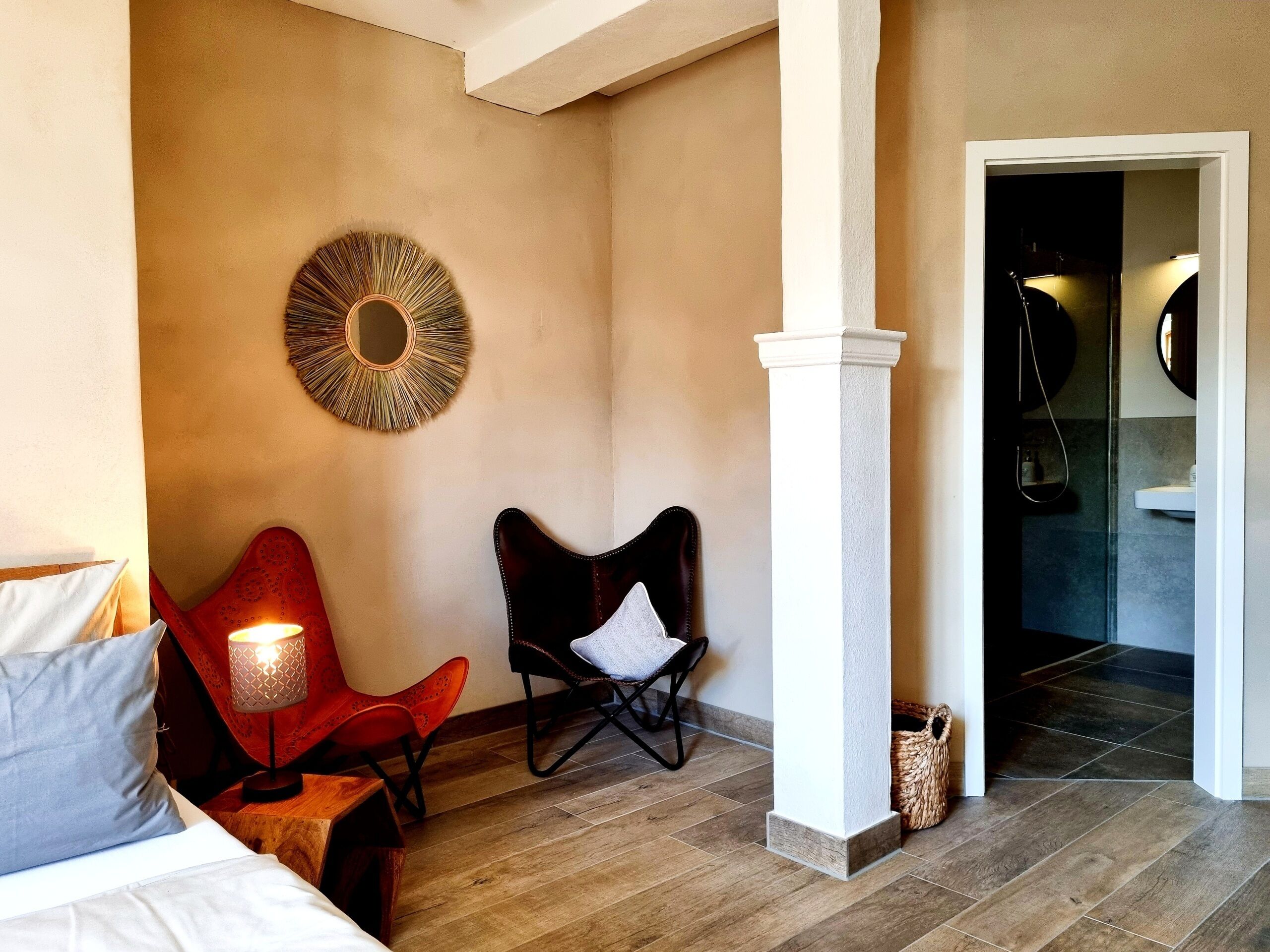 Ein Hotelzimmer mit einem Bett, zwei Sesseln, einem wandmontierten Spiegel und einem durchgegangene Tür einsehbarer Badezimmer.
