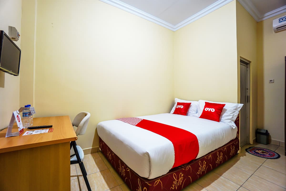 A hotel room with a bed, a desk, a chair, a TV, and a door.