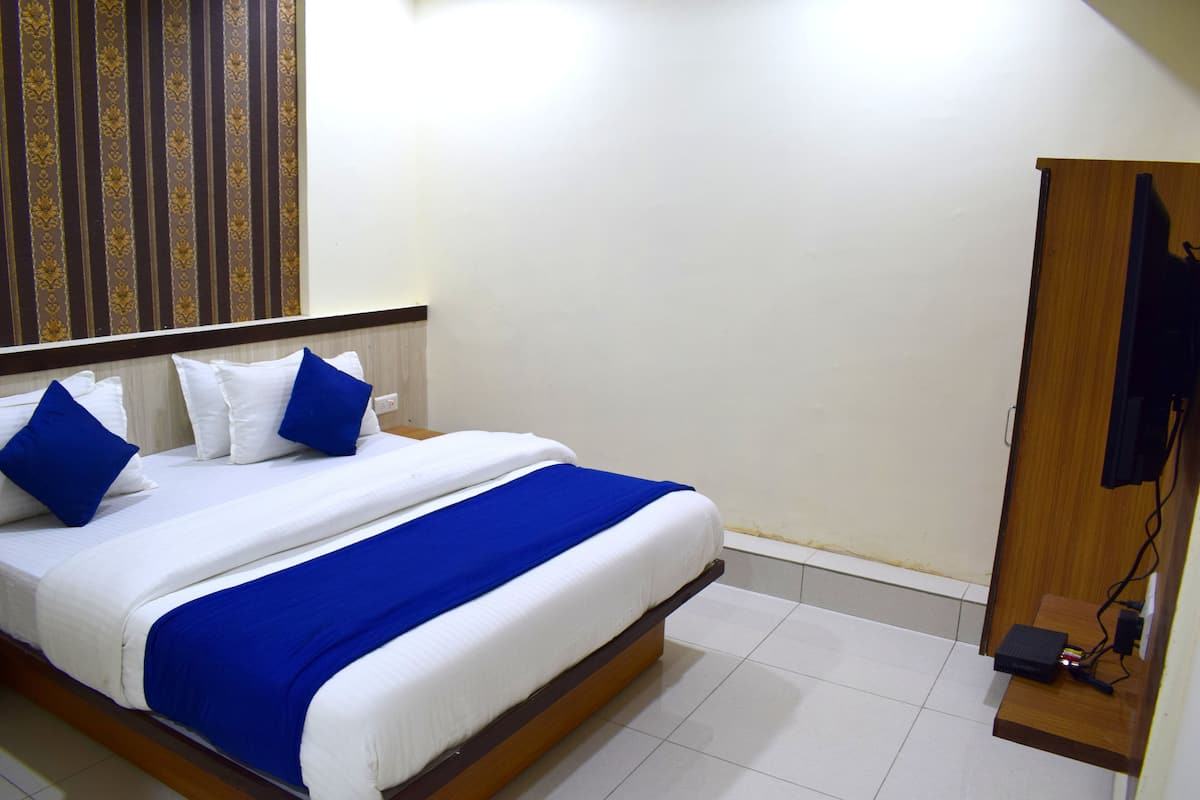 A neatly made bed with white and blue bedding, a wooden headboard, and a wall-mounted television.