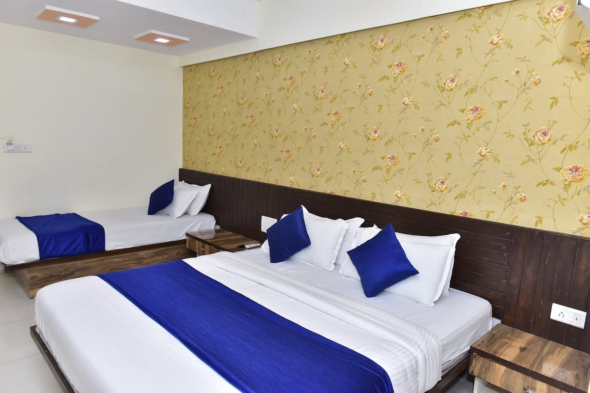 A hotel room with two beds, each with white bedding and blue accents, a wooden headboard, and a floral wallpaper design.