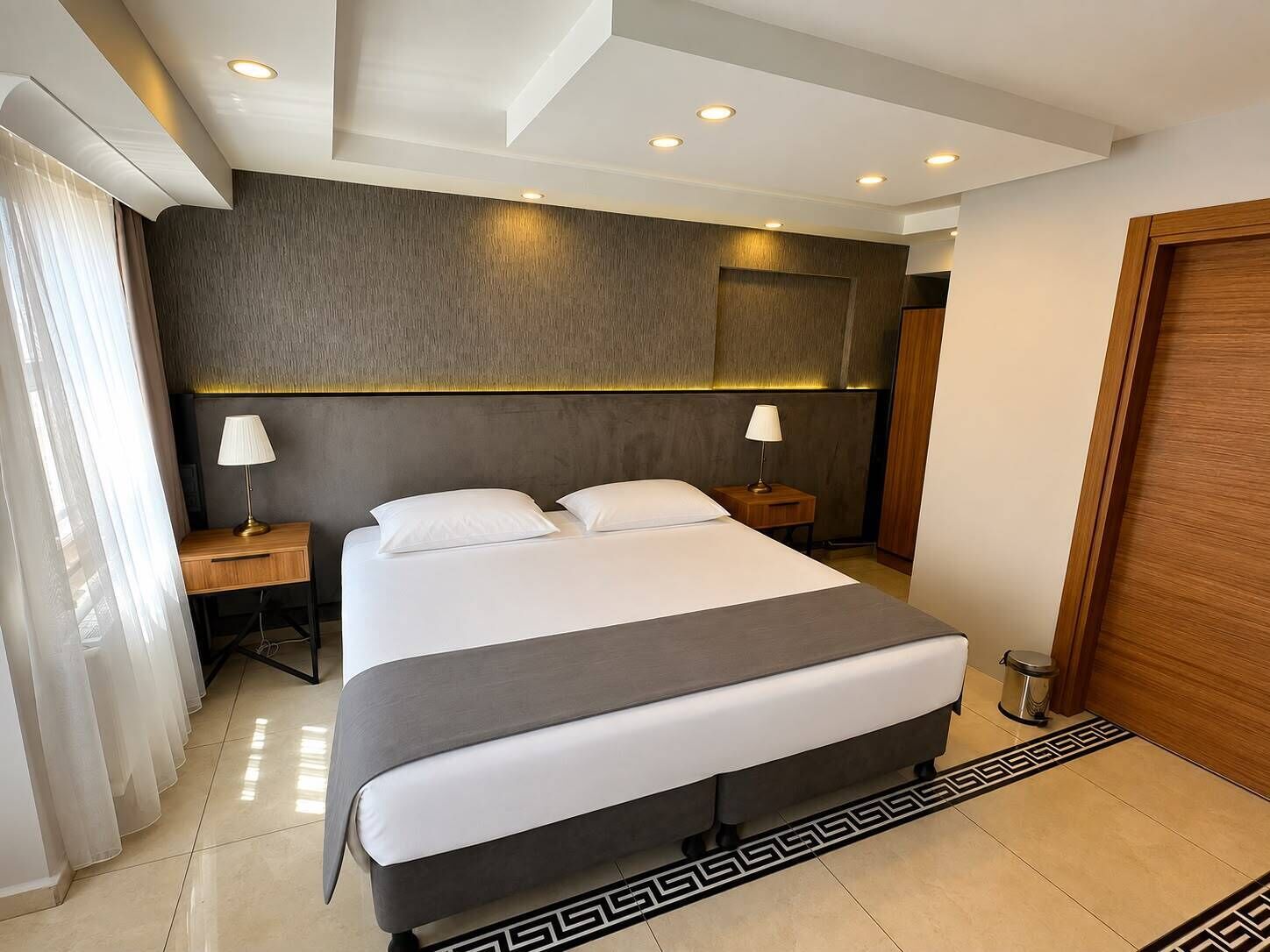 A modern hotel room with a large bed, two bedside tables with lamps, a wooden wardrobe, and a decorative floor pattern.