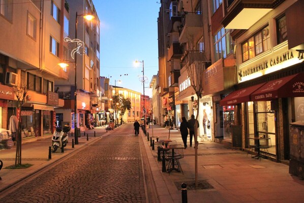 A cobblestone street lined with buildings, some with signage indicating shops and cafes. - Degirmenlik Casamia Suite (Çanakkale)