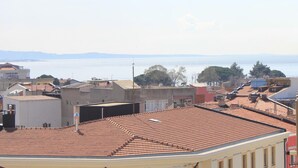 A coastal cityscape with terracotta-tiled rooftops, buildings with balconies, and a view of the sea and distant mountains. - Degirmenlik Casamia Suite (Çanakkale)