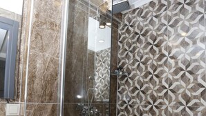 A modern bathroom with a glass-enclosed shower, a marble-tiled wall, and a geometric-patterned tile backsplash. - Degirmenlik Casamia Suite (Çanakkale)