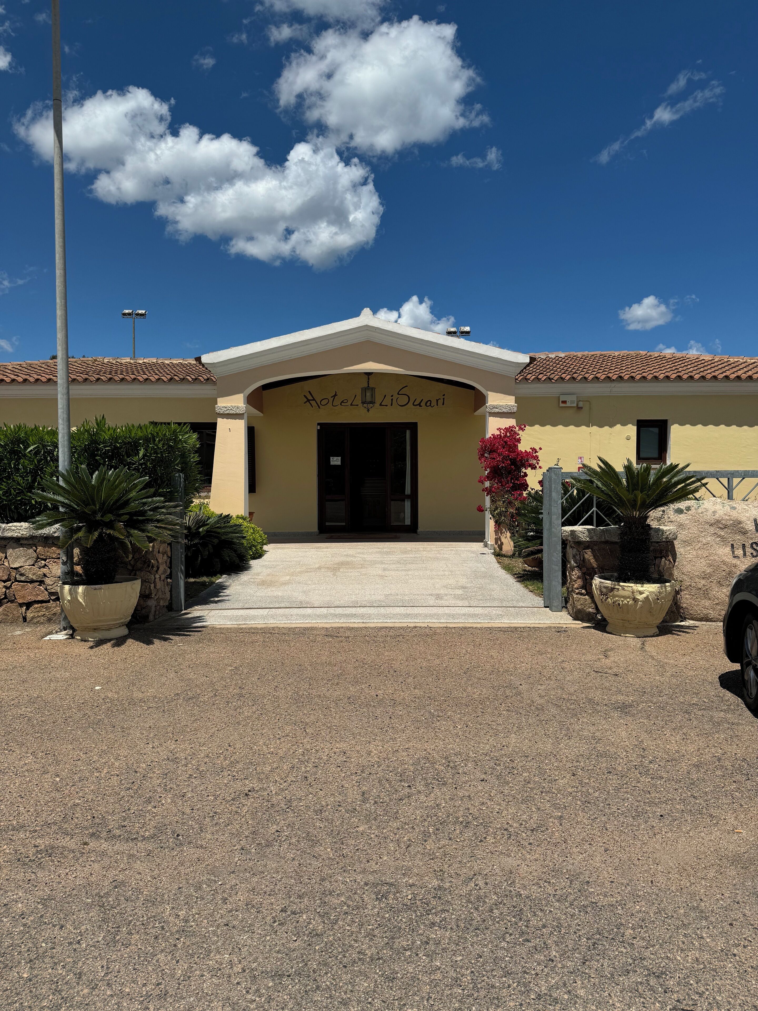 A hotel entrance with a clear sky, a tiled roof, and a sign reading "Hotel LiSuari".