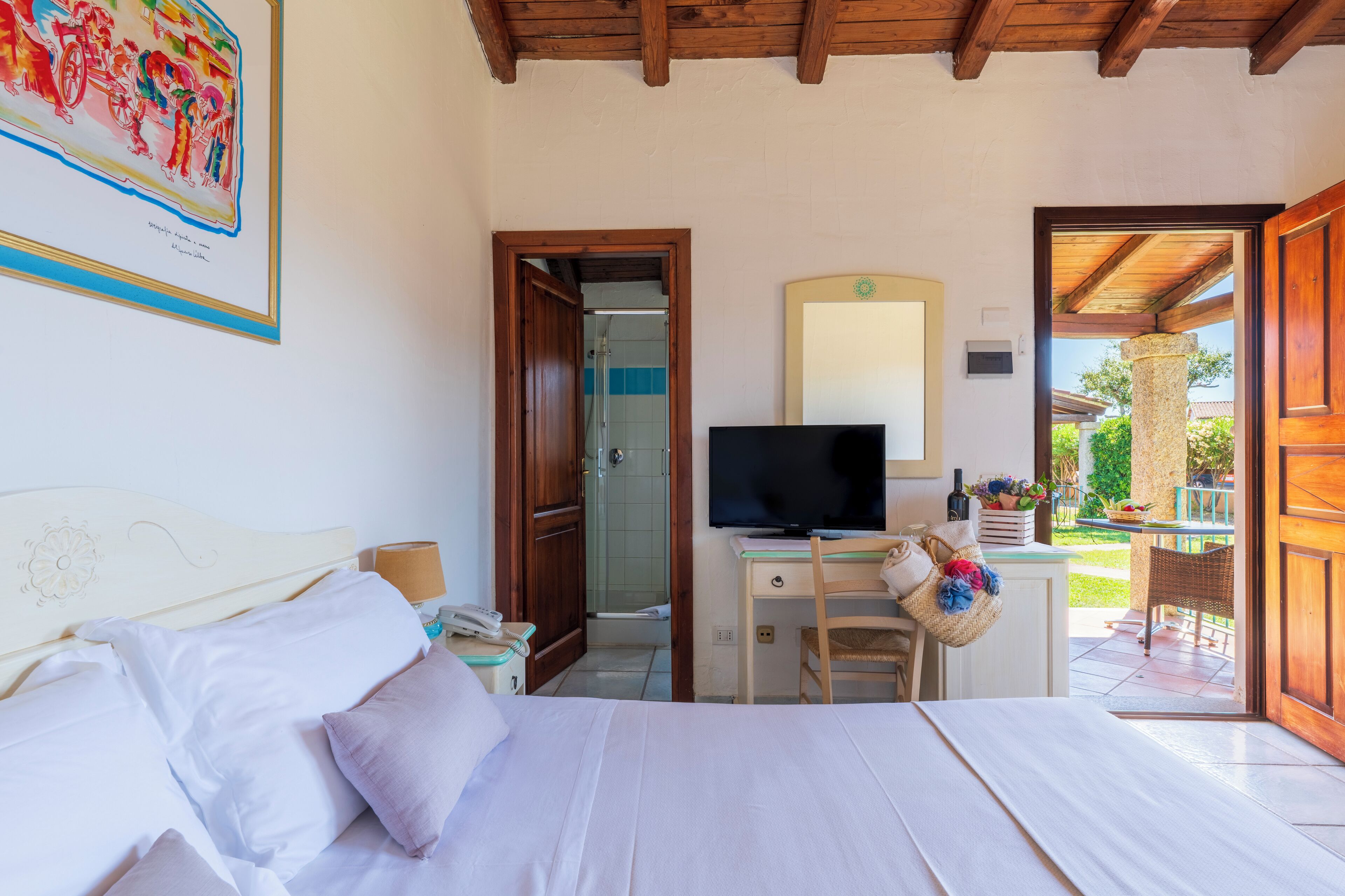 Een slaapkamer met een bed, een bureau met een computer, een televisie en een deur naar een balkon.