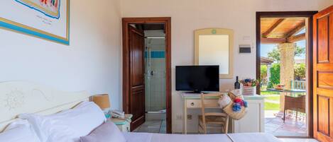 Een slaapkamer met een bed, een bureau met een computer, een televisie en een deur naar een balkon.