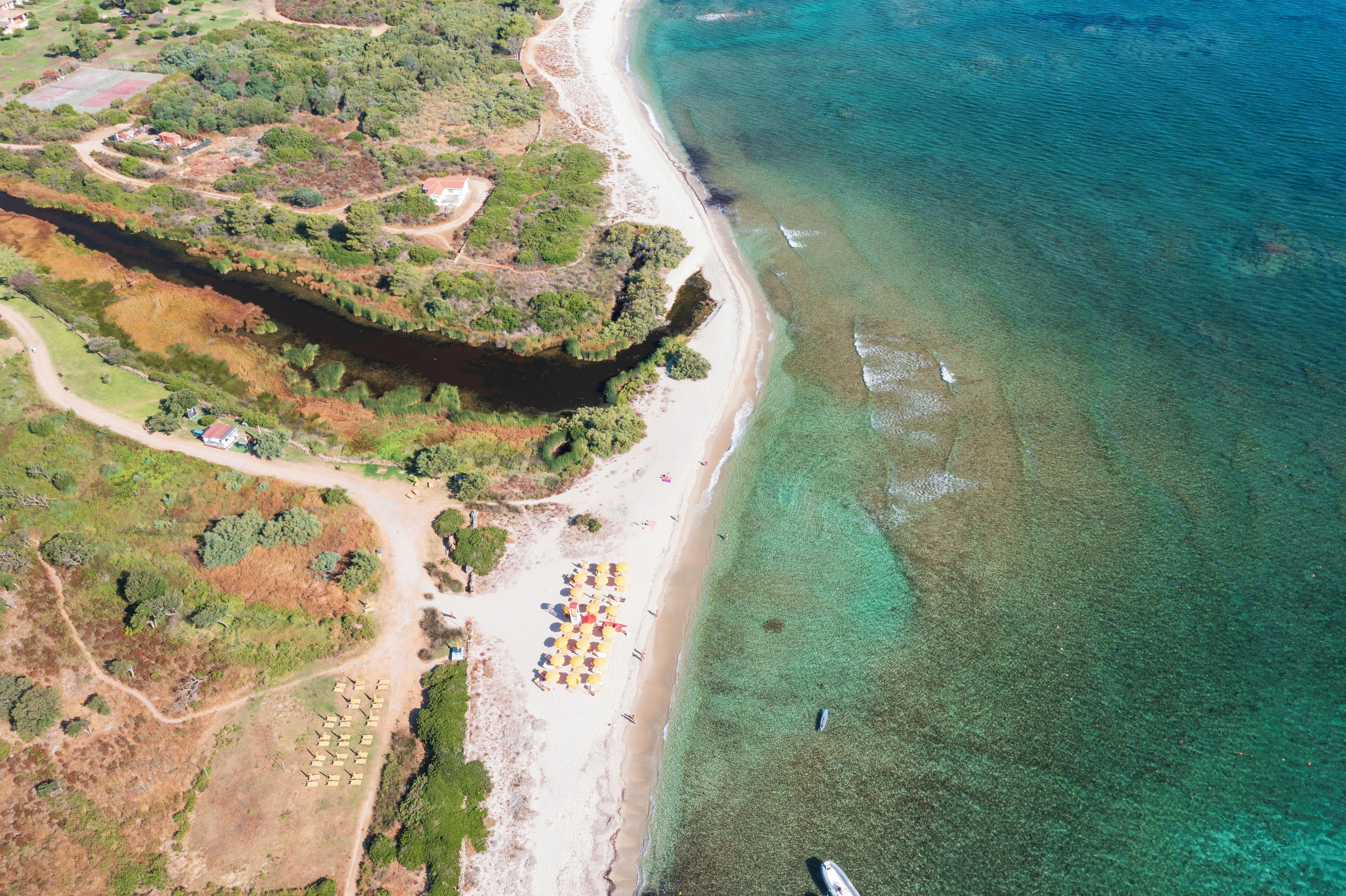 An aerial view of a beach with clear waters, a sandy shore, and a few umbrellas.