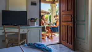Une pièce avec un bureau en bois, un téléviseur et une vue sur deux personnes dînant à l’extérieur.