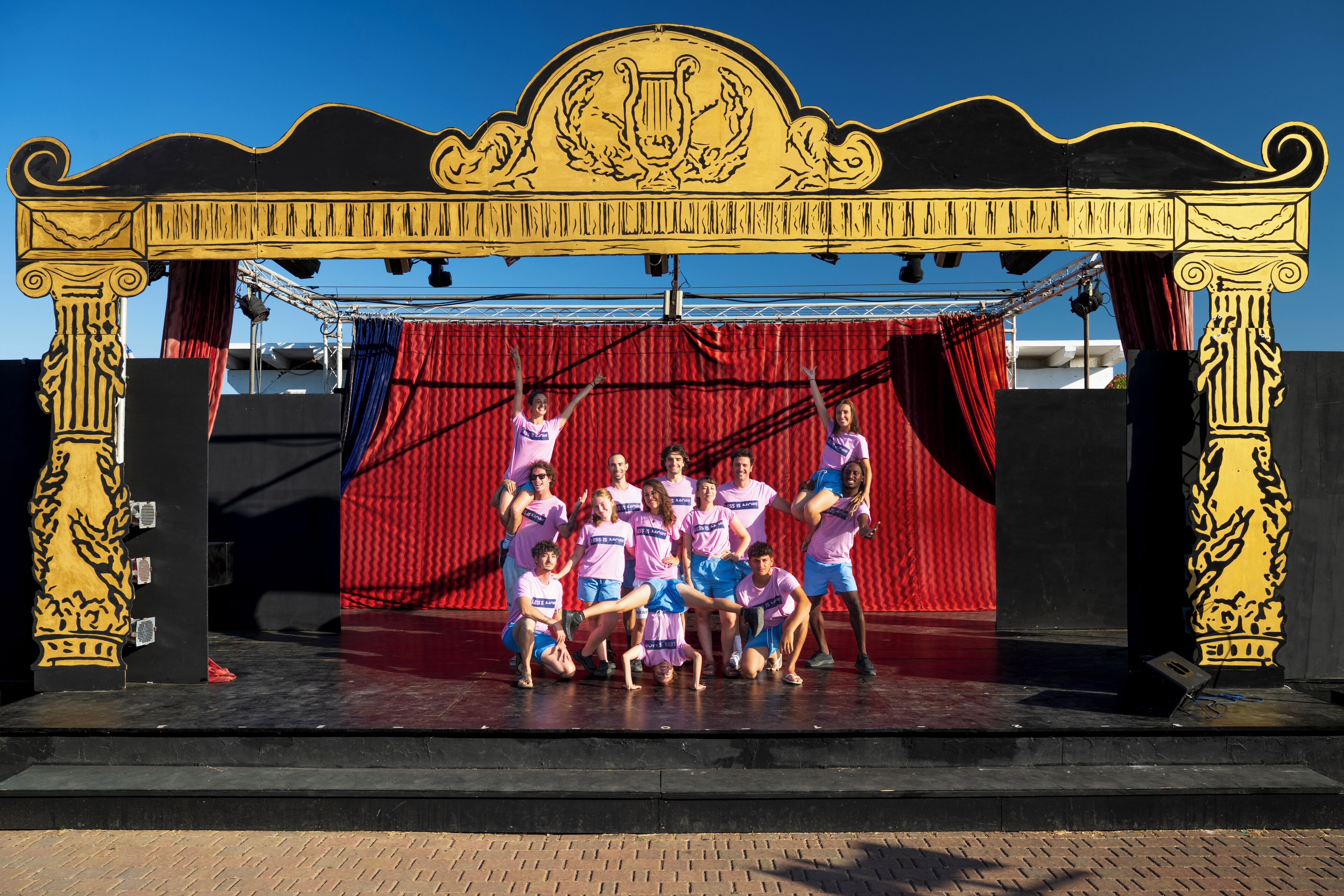 A stage with a group of people in matching outfits, a red curtain backdrop, and ornate black and gold architectural elements.