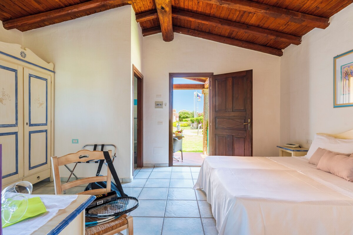 Une chambre à coucher comprenant un lit, une chaise, une petite table et une porte donnant sur un espace extérieur.