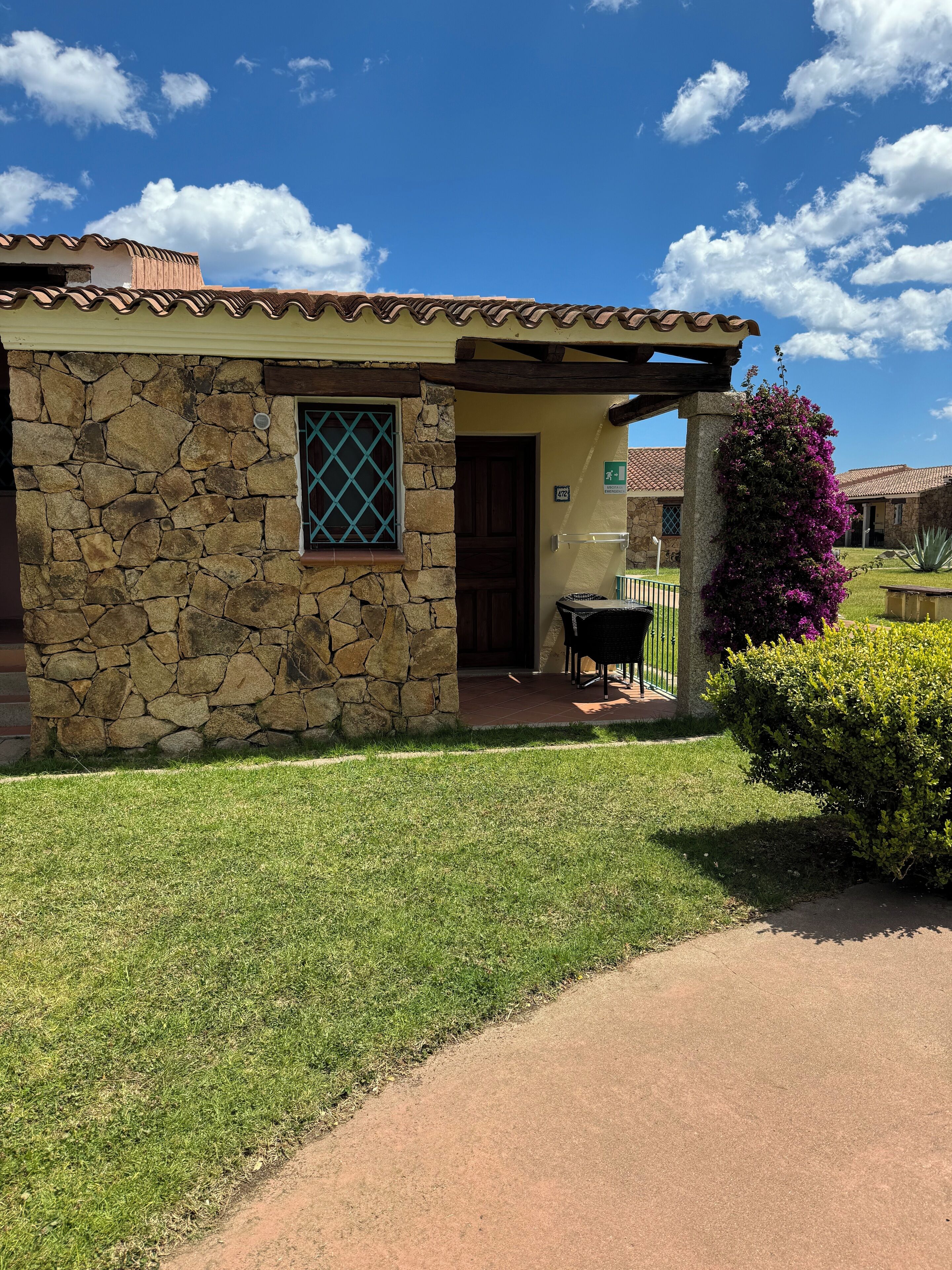 A stone house with a tiled roof, a small porch, and a well-maintained lawn.