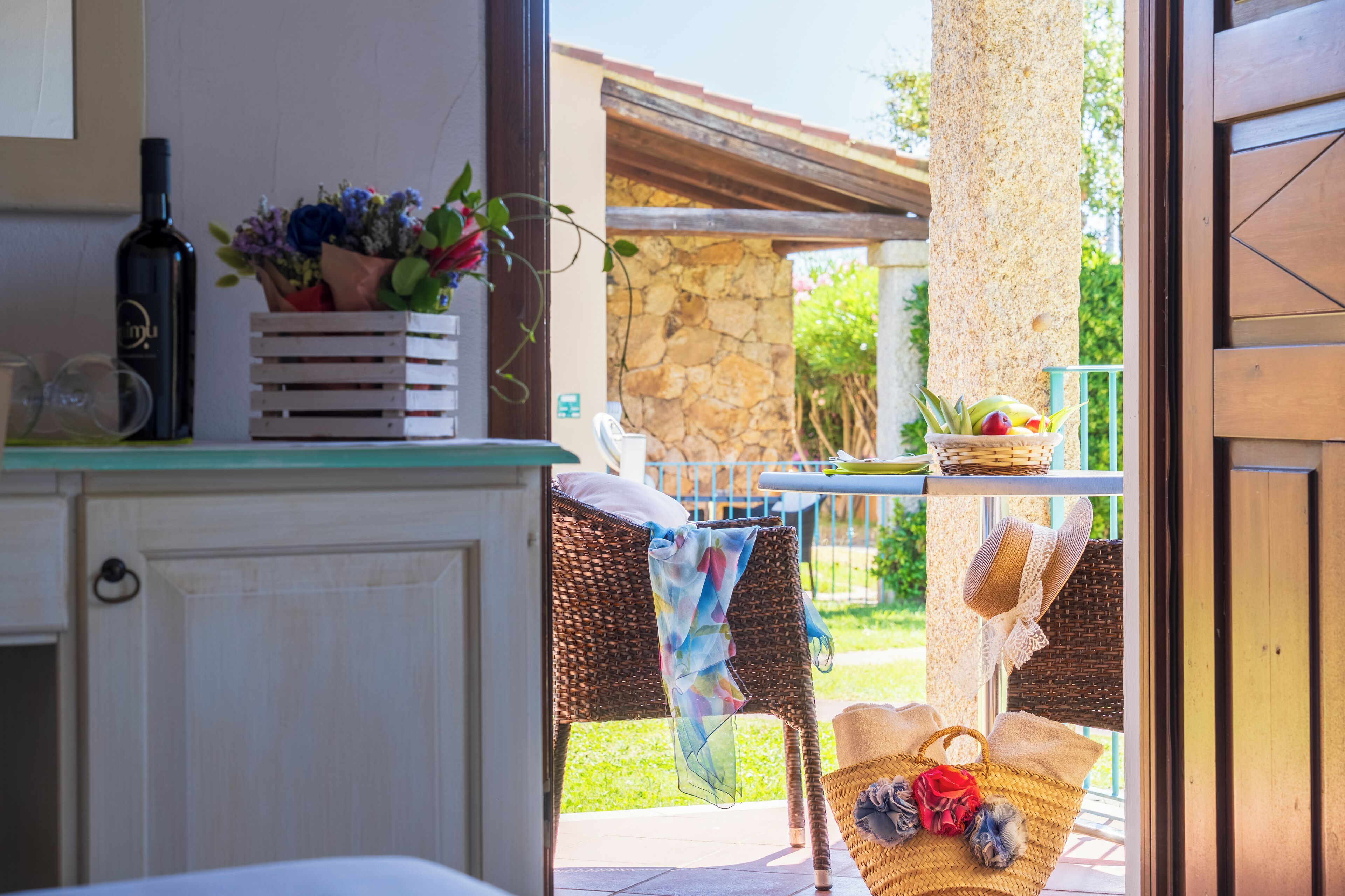 Un rincón de cocina con una botella de vino, una silla de mimbre y una cesta de frutas.