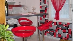 A modern kitchen with white cabinets, a red and black patterned backsplash, and a red curtain. There are two red bar stools and a white countertop with a wine glass. - Apartments Sikirica 1 (Trogir)
