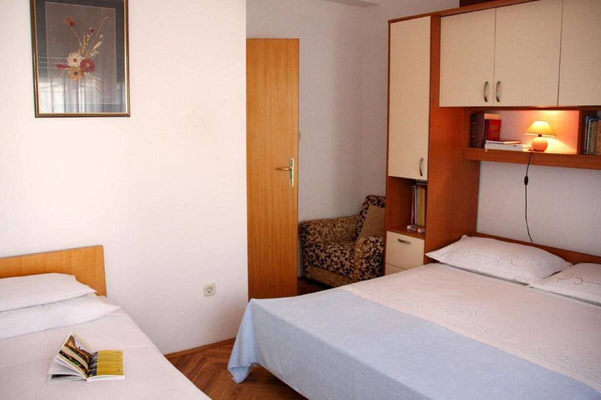 A bedroom with two beds, a wardrobe, a bedside table with a lamp, and a framed picture on the wall.