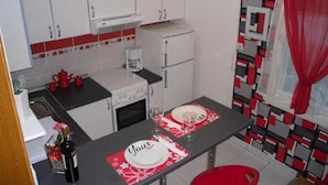 A compact kitchen with white cabinets, a coffee maker, and a dining table set for two with a red and white table runner. - Apartments Sikirica 1 (Trogir)