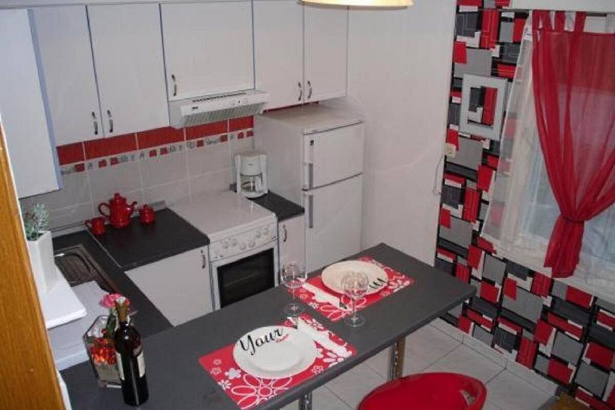 A compact kitchen with white cabinets, a coffee maker, and a dining table set for two with a red and white table runner.
