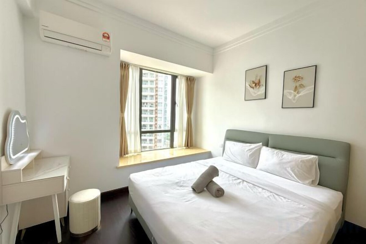 A hotel room with a bed, a desk, a chair, a window with curtains, and two framed pictures on the wall.