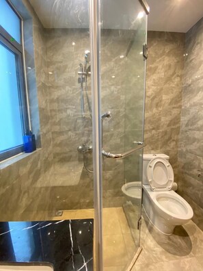 A modern bathroom with a glass-enclosed shower, a toilet, and a marble-tiled floor.