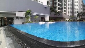 A swimming pool with a tiled edge, surrounded by a landscaped area with palm trees and a building in the background. - R&F Princess Cove by Wong (Johor Bahru)