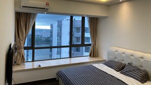 A hotel room with a large window, a bed with striped bedding, a flat-screen TV, and an air conditioning unit. - R&F Princess Cove by Wong (Johor Bahru)