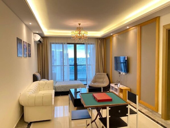 A modern hotel room with a bed, a sofa, a TV, and a table with a book.