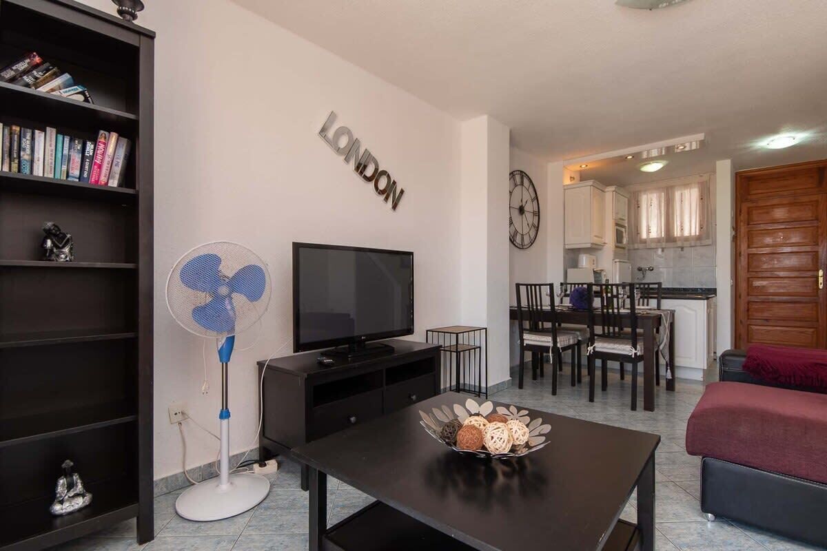 Una sala moderna con televisor de pantalla plana, un ventilador y un comedor con un reloj en la pared.
