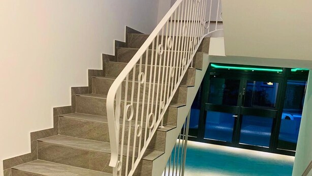 A staircase with a white railing leading to a balcony with a glass door and a pool. - Checkinn Hotel (Bad Salzuflen)