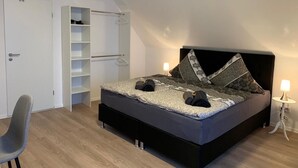 A bedroom with a bed, a wardrobe, a chair, and a bedside table. - Checkinn Hotel (Bad Salzuflen)