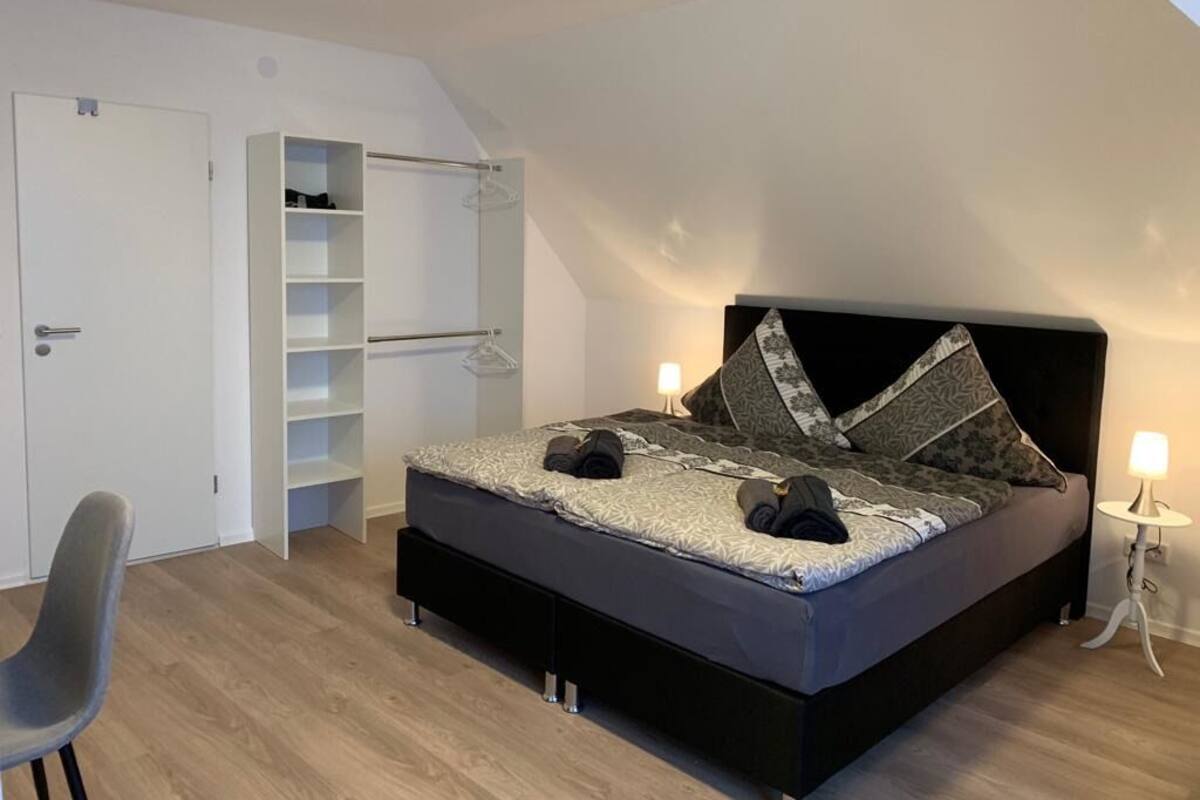 Une chambre à coucher avec un lit, une armoire, une chaise et une table de chevet.