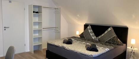Een slaapkamer met een bed, een kledingkast, een stoel en een nachtkastje.
