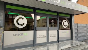 A Check Inn Hotel entrance with a modern design, featuring a prominent logo and bilingual welcome signs. - Checkinn Hotel (Bad Salzuflen)