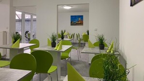 A modern dining area with green chairs and tables, potted plants, and a painting on the wall. - Checkinn Hotel (Bad Salzuflen)