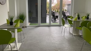 A modern indoor dining area with a large sliding glass door leading to an outdoor patio. - Checkinn Hotel (Bad Salzuflen)
