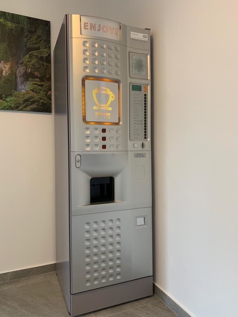 A coffee machine with a cup icon, a menu, and a coin slot.