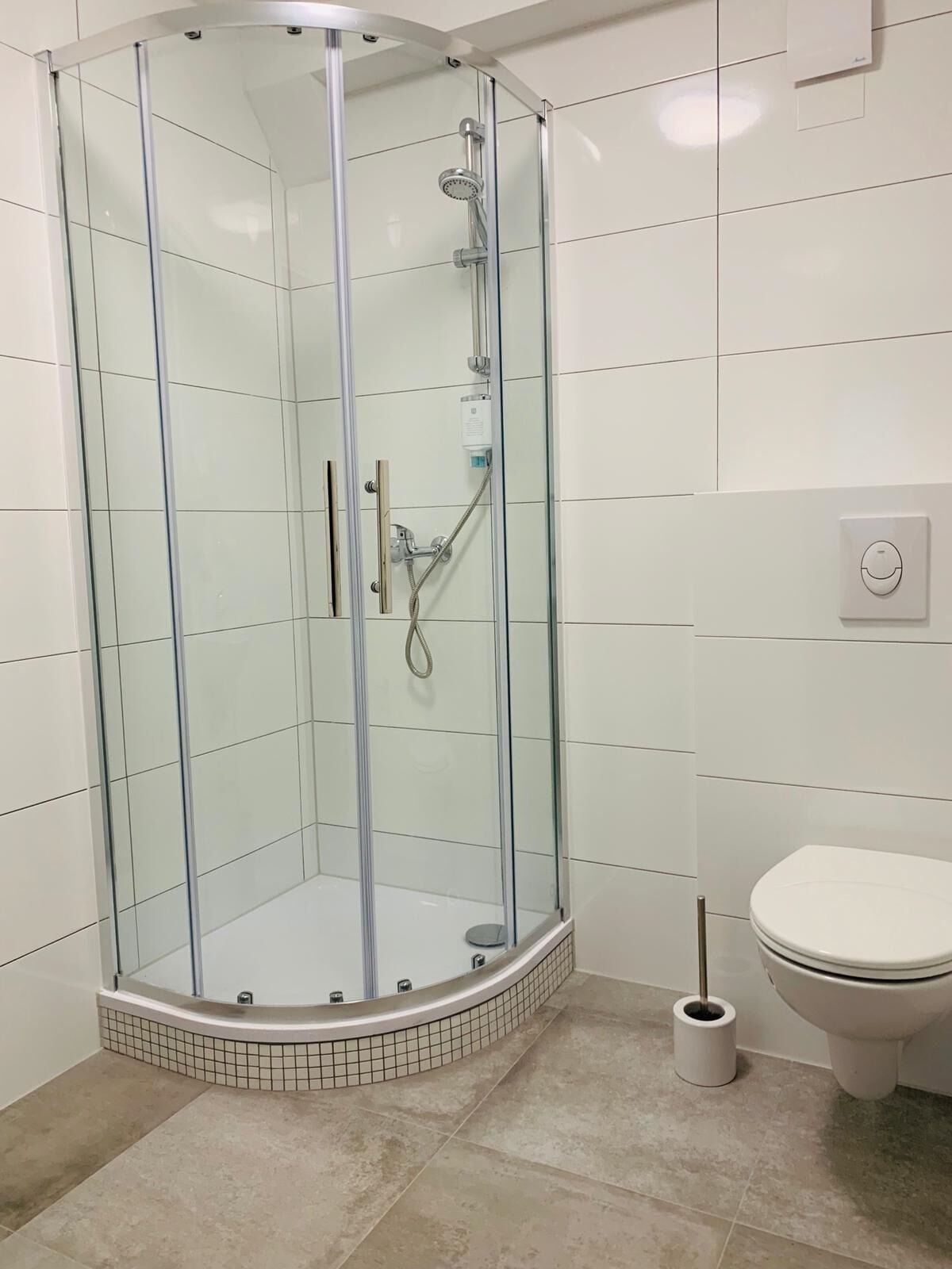 Ducha con mampara de vidrio, inodoro y bidé a la derecha.