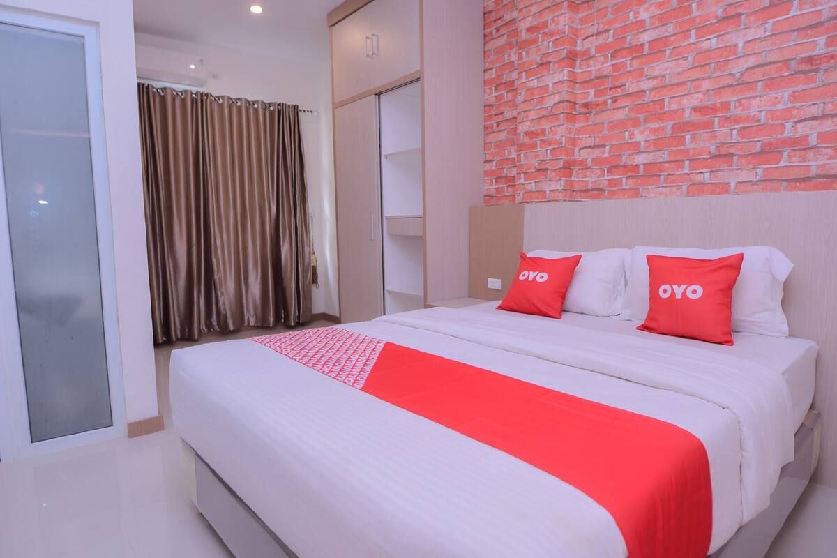 A hotel room with a bed, a red and white bedspread, and a brick-patterned wall.