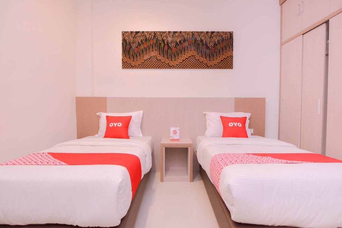 A hotel room with two beds, each with a red and white bedspread, and a small bedside table with a sign.