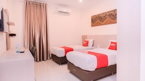 Une chambre d’hôtel avec deux lits, un bureau, une bouteille d’eau, un climatiseur et un tableau au mur.