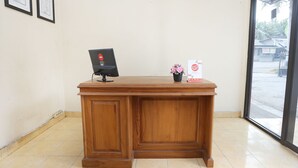 A wooden reception desk with a computer monitor and a small vase of flowers. - Hotel O Penginapan Kepurun Pawana Indonesia (Cangkringan)