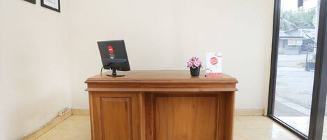 A wooden reception desk with a computer monitor and a small vase of flowers.