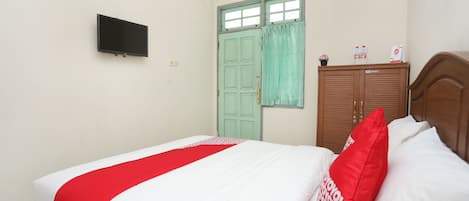 A bedroom with a bed, a television on the wall, a green door, and a wooden wardrobe.