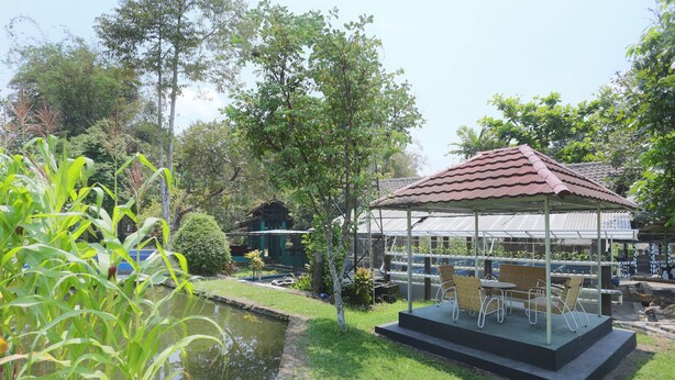 A garden with a pond, a gazebo with outdoor seating, and a building with a tiled roof in the background. - Hotel O Penginapan Kepurun Pawana Indonesia (Cangkringan)