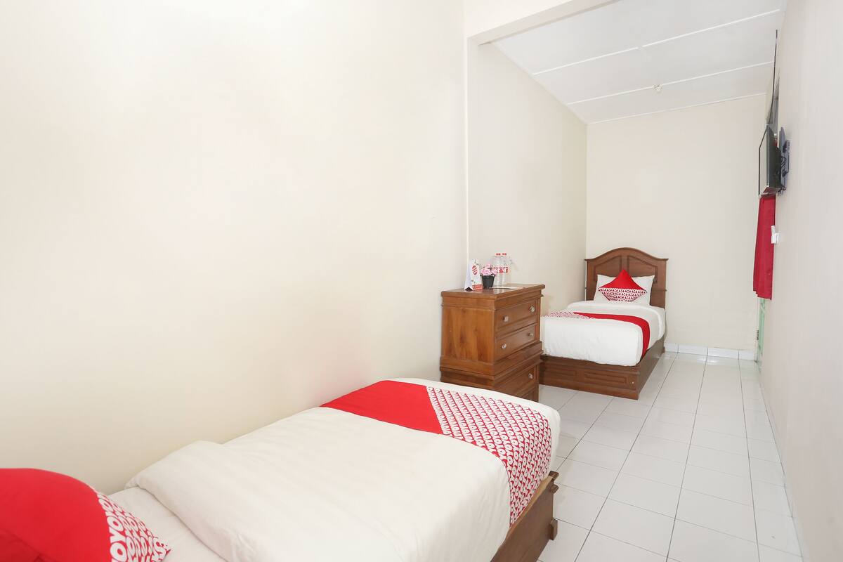 Une chambre avec deux lits, une commode en bois et un téléviseur fixé au mur.