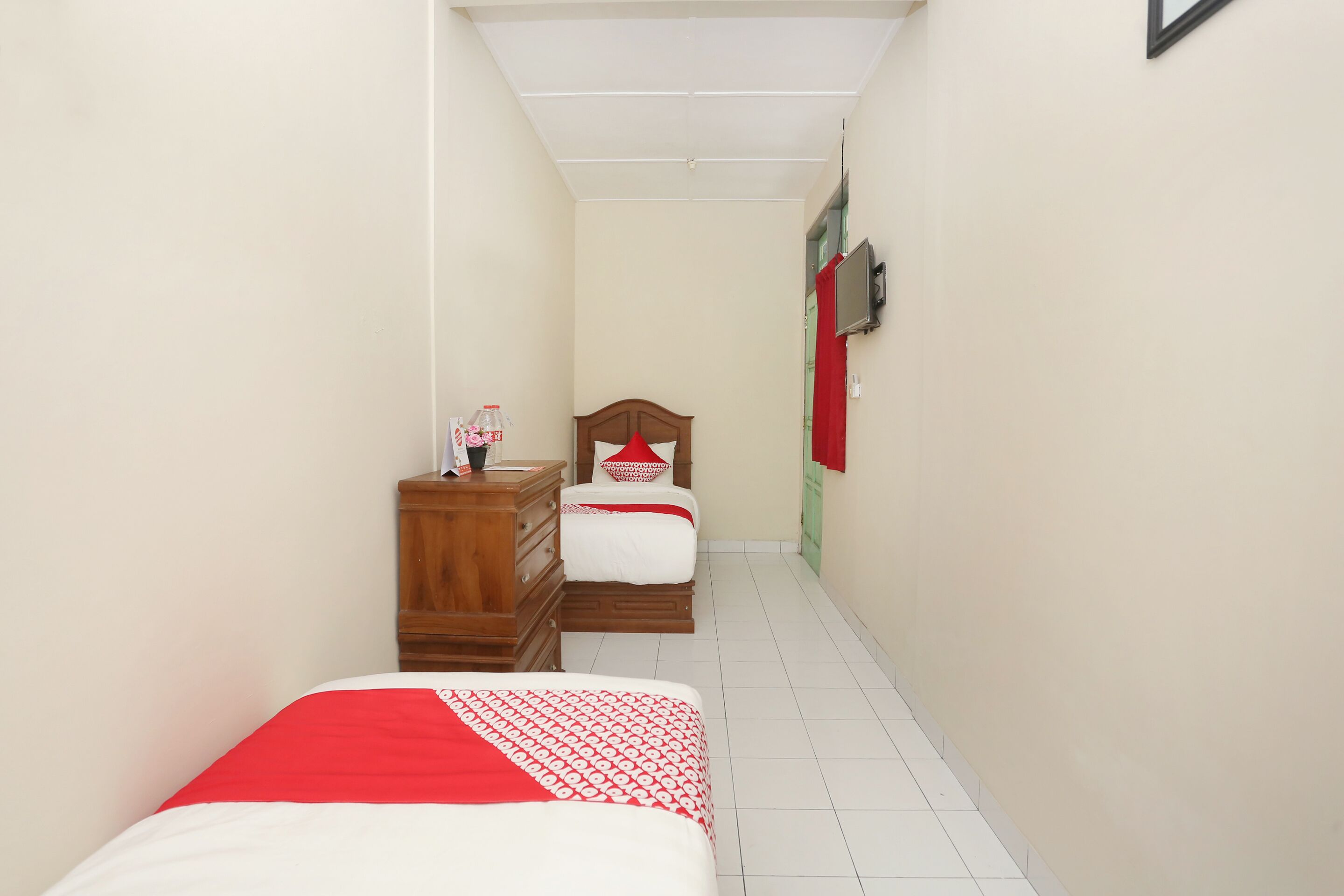Un couloir étroit, avec un lit sur la gauche et une commode avec un miroir sur la droite.