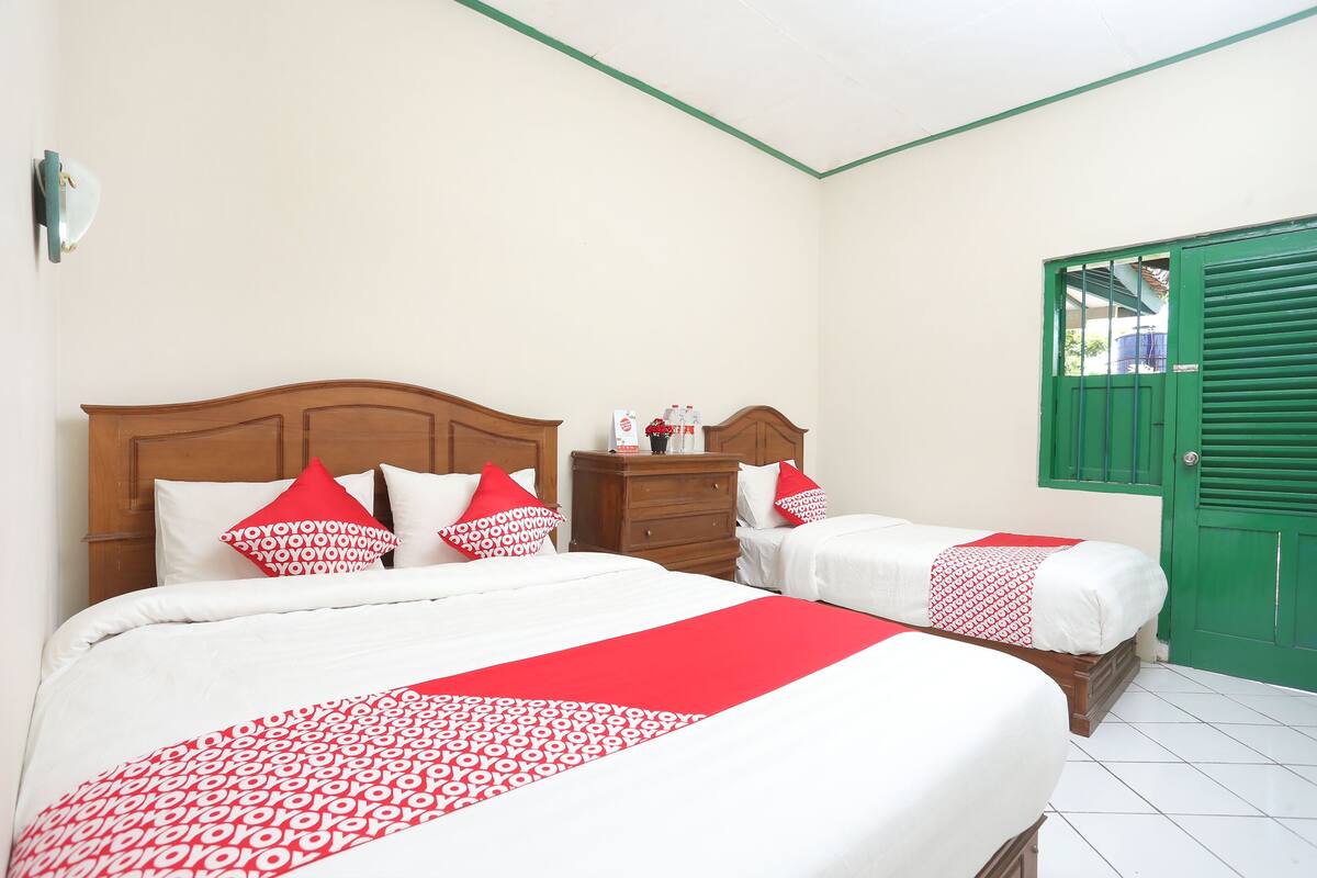 Une chambre d’hôtel avec deux lits, une tête de lit en bois, une porte verte et un sol carrelé.
